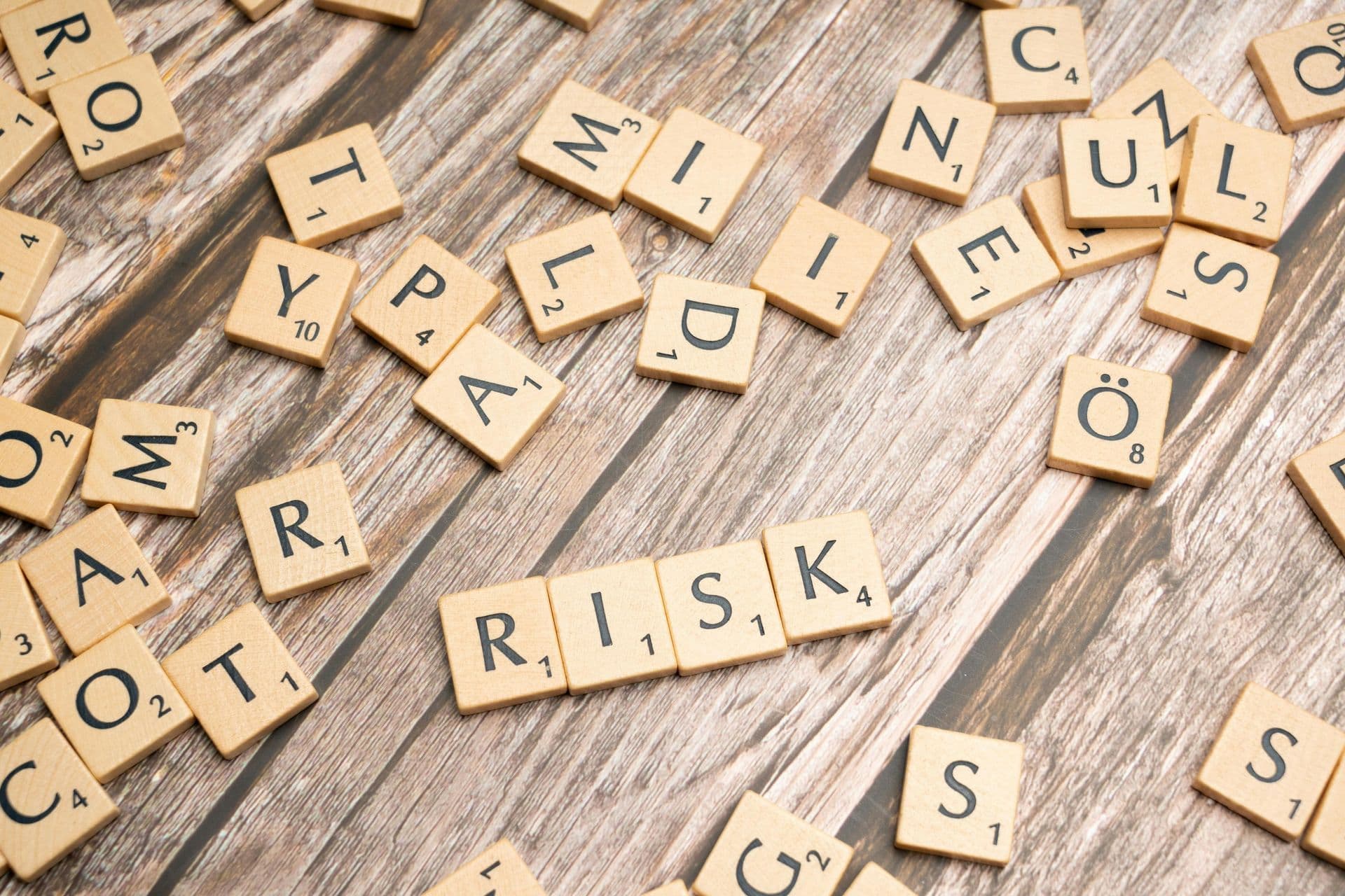 Wooden letter tiles on a table, with the word RISK spelled out in the middle.