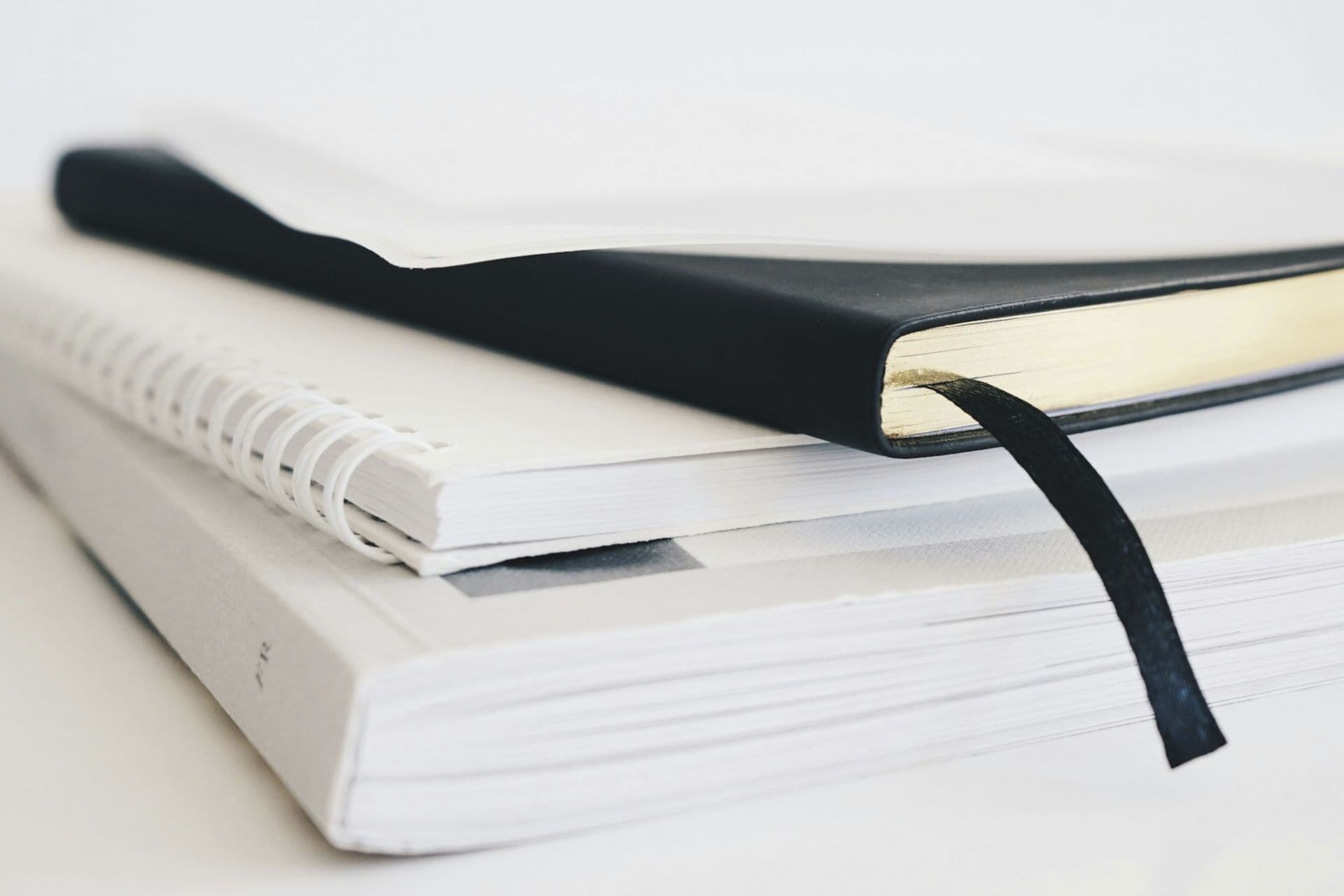 A black book is sitting on top of a stack of white books.