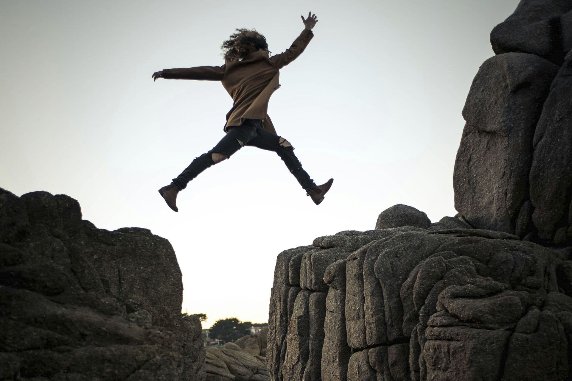 A person leaping across a gap between two rocks.