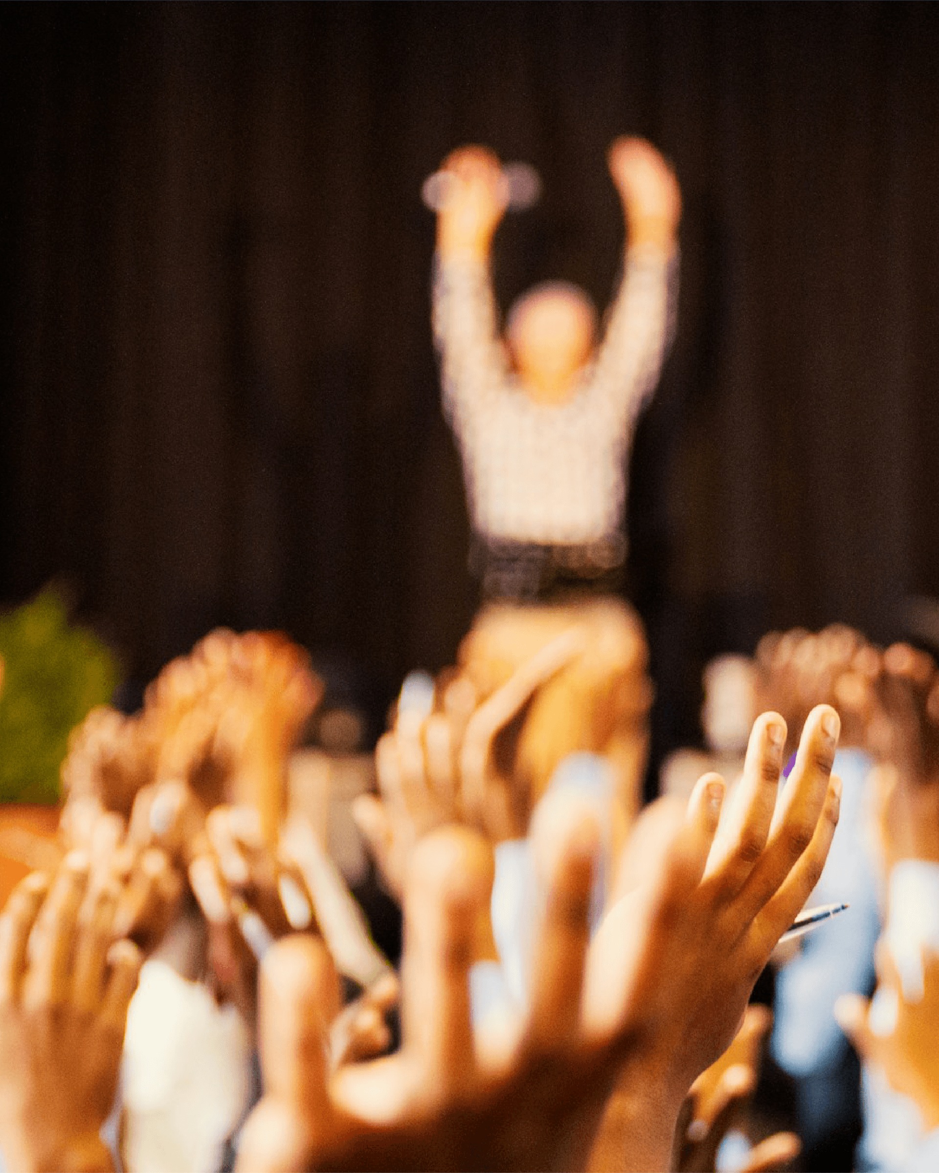 Hands raised toward a blurred figure on stage, holding microphones.